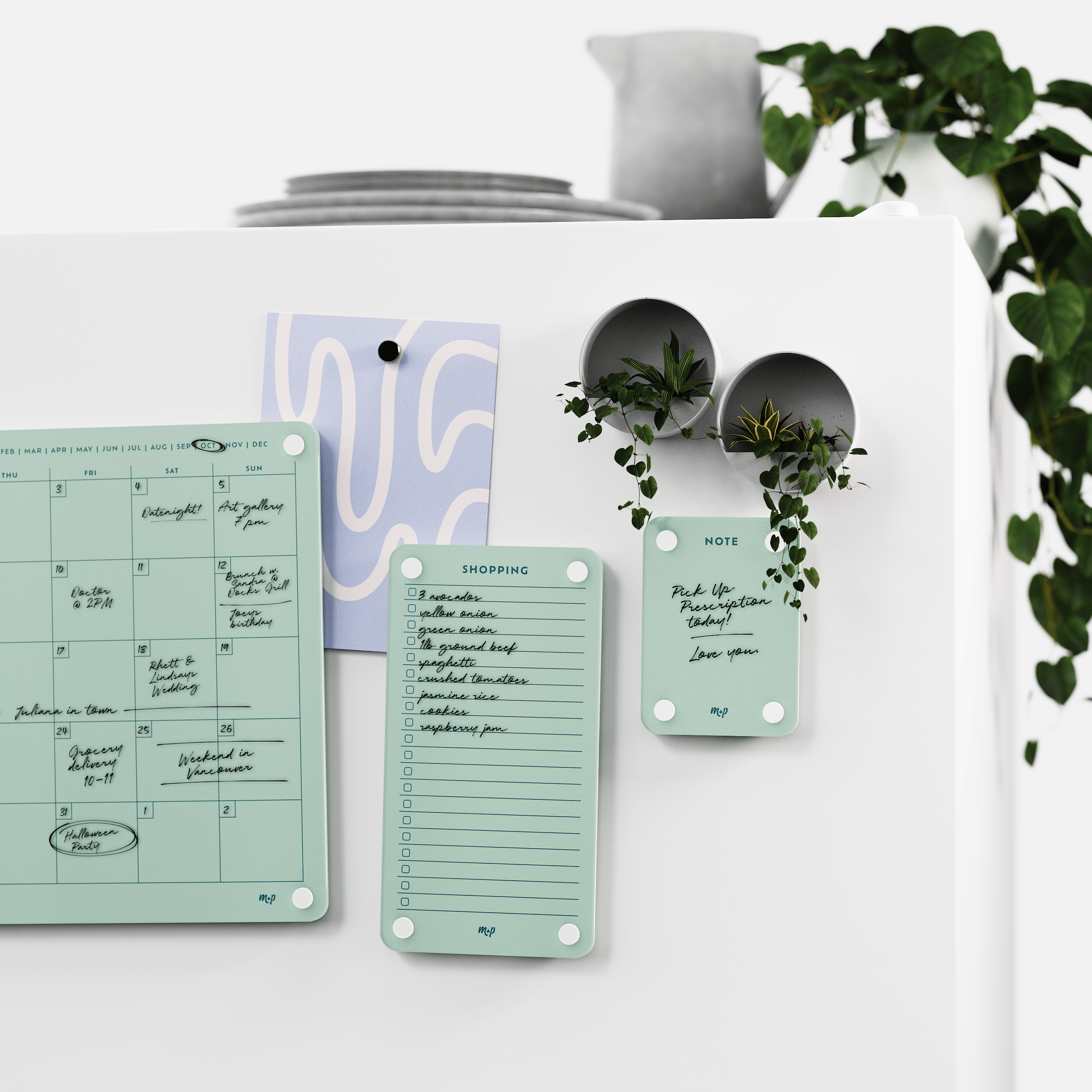 Seafoam green calendar, shopping list and note board on a white wall beside two magnetic planters